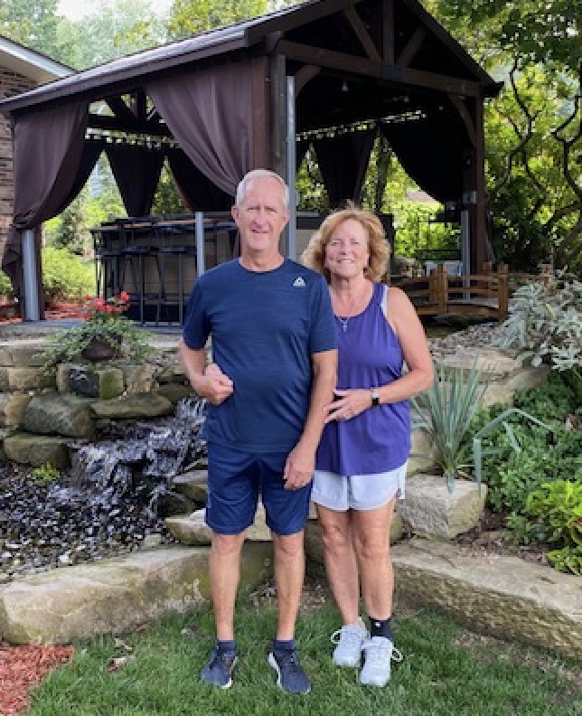 A couple standing in front of a gazebo in their backyard.