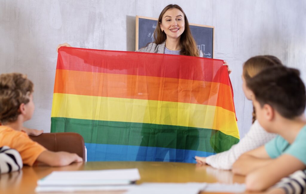 A teacher holds up a rainbow flag in front of a group of students.