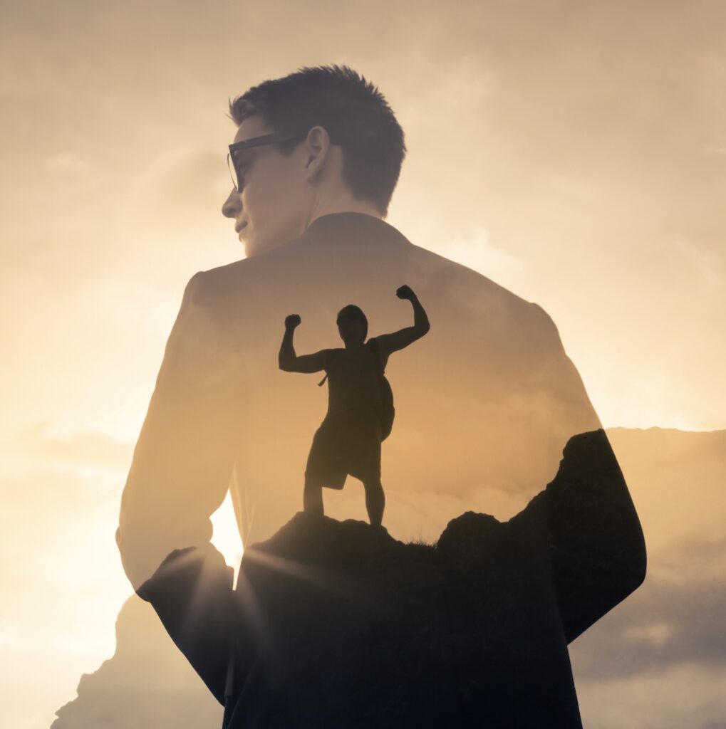 A silhouette of a man standing on top of a mountain.