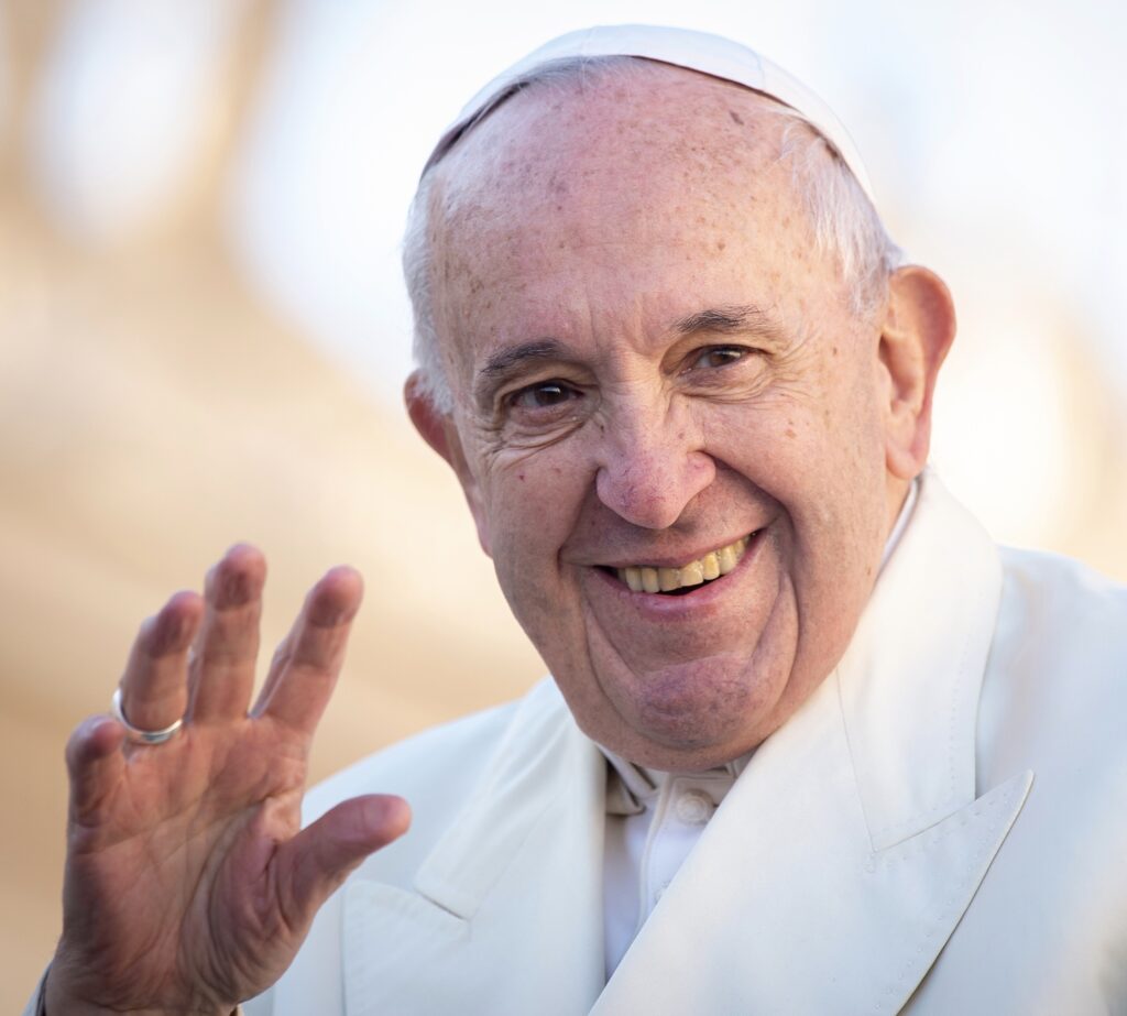 A smiling pope waving his hand.