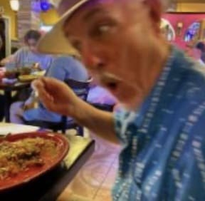 A man wearing a hat and blue shirt eats food