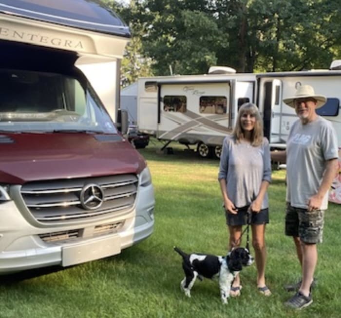 Couple with dog near camper vans outdoors.