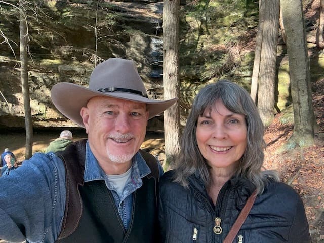 Smiling couple in forested outdoor setting.